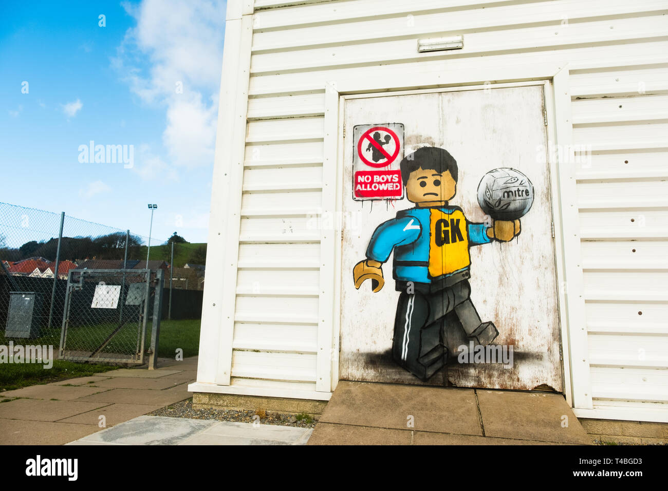 'No Boys Allowed' Graffiti by James Ame - Ame72 (The `Lego Guy)  -  on the exterior of the leisure centre in Aberystwyth, showing an unhappy boy in a GK  netball vest, in reference to the ban by the Urdd ( a welsh langiage youth organisation) on boys competing in netball competitions.  March 10 2019 Stock Photo